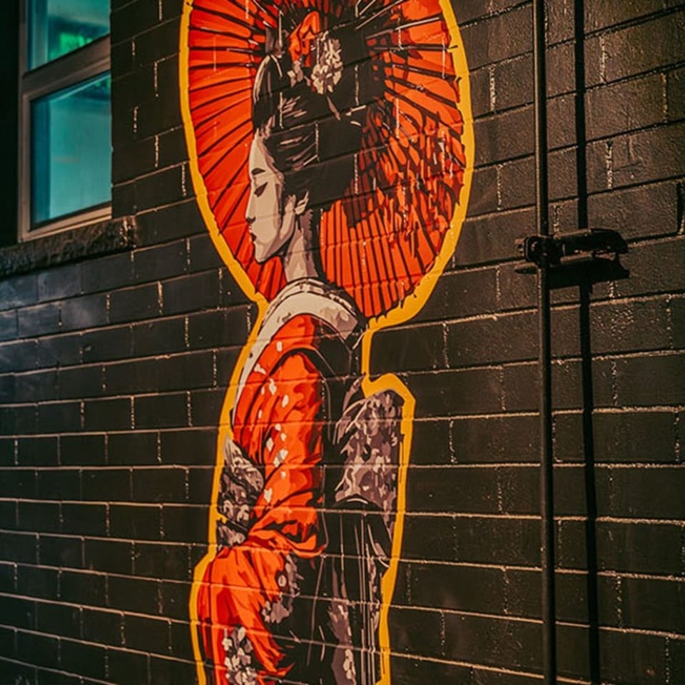 Vibrant mural of a woman in a red kimono and umbrella on a dark brick wall.