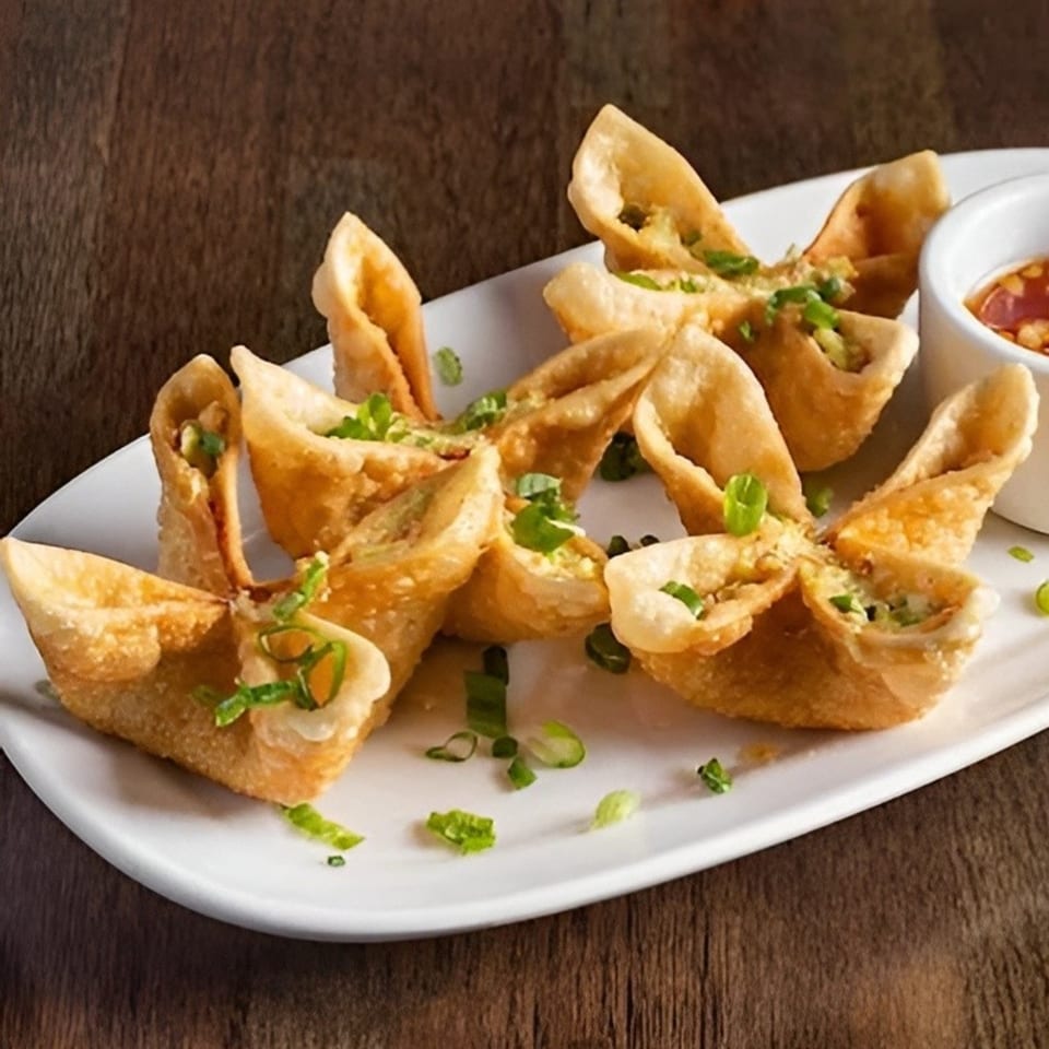 Crispy crab rangoon appetizers, garnished with green onions, served on a white plate with dipping sauce.