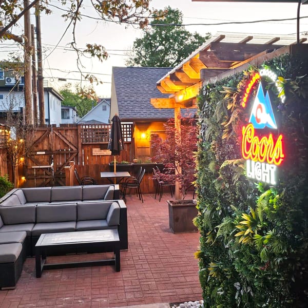Outdoor patio with a large sectional sofa, tables, chairs, and a glowing Coors Light neon sign.