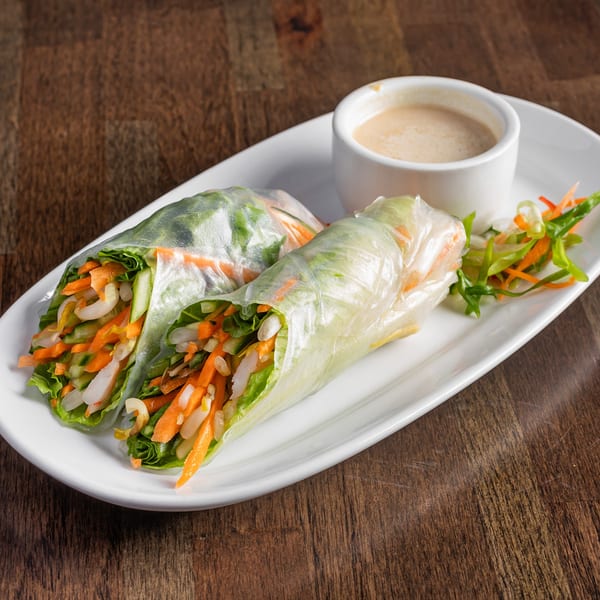 Two fresh spring rolls with vegetables and shrimp, served with peanut sauce on a white plate.