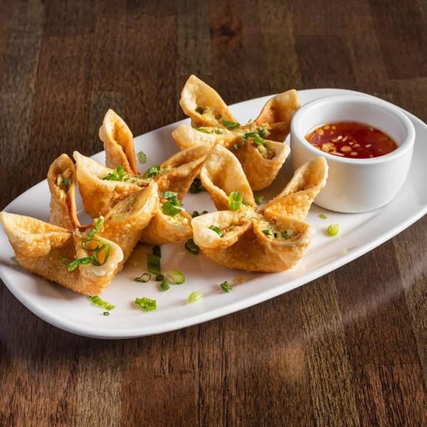 Crispy crab rangoon appetizers with green onions and a side of sweet chili dipping sauce.