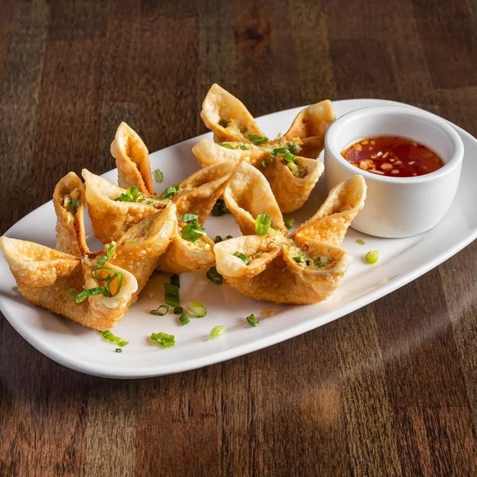 Crispy crab rangoon appetizers with green onions and a side of sweet chili dipping sauce.