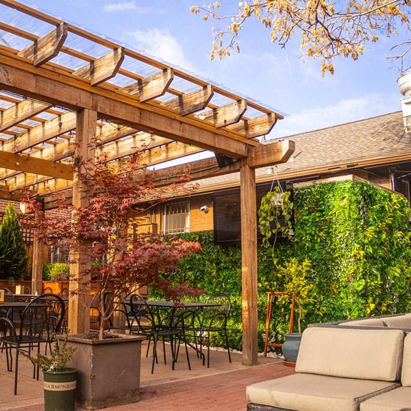 An outdoor patio with a wooden pergola, black tables and chairs, and a lush green living wall.