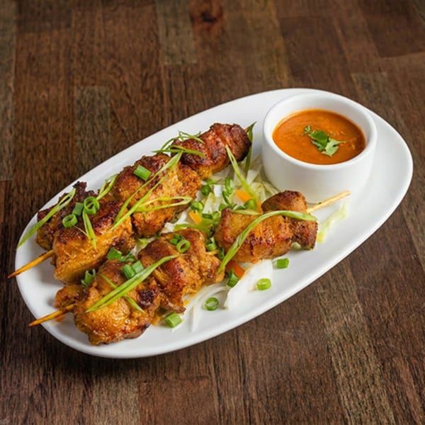 Chicken satay skewers with peanut sauce and green onions on a white plate.