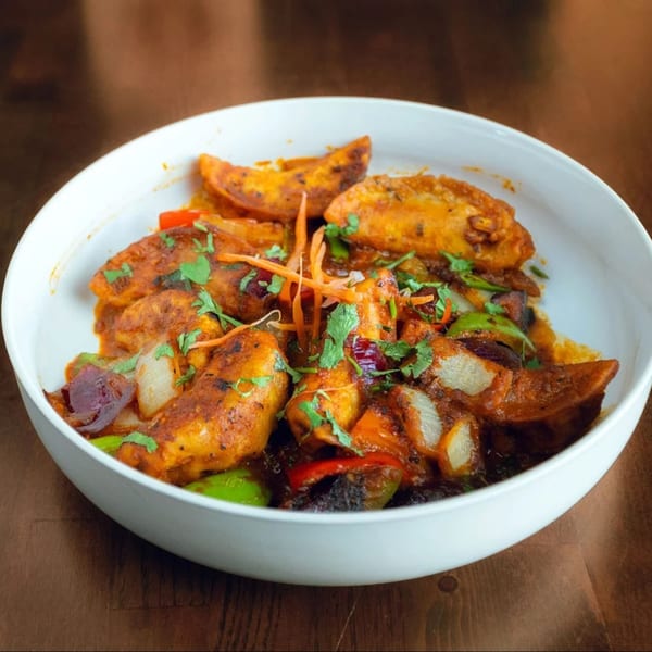 Spicy potato wedges with bell peppers, onions, and cilantro in a white bowl.